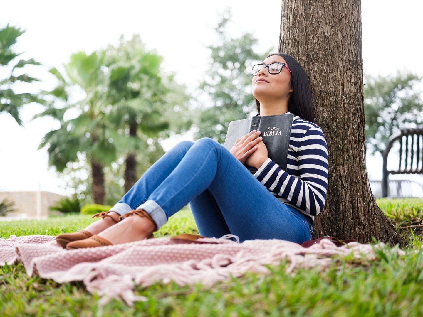 Pretty young woman sitting next to tree and holding Bible