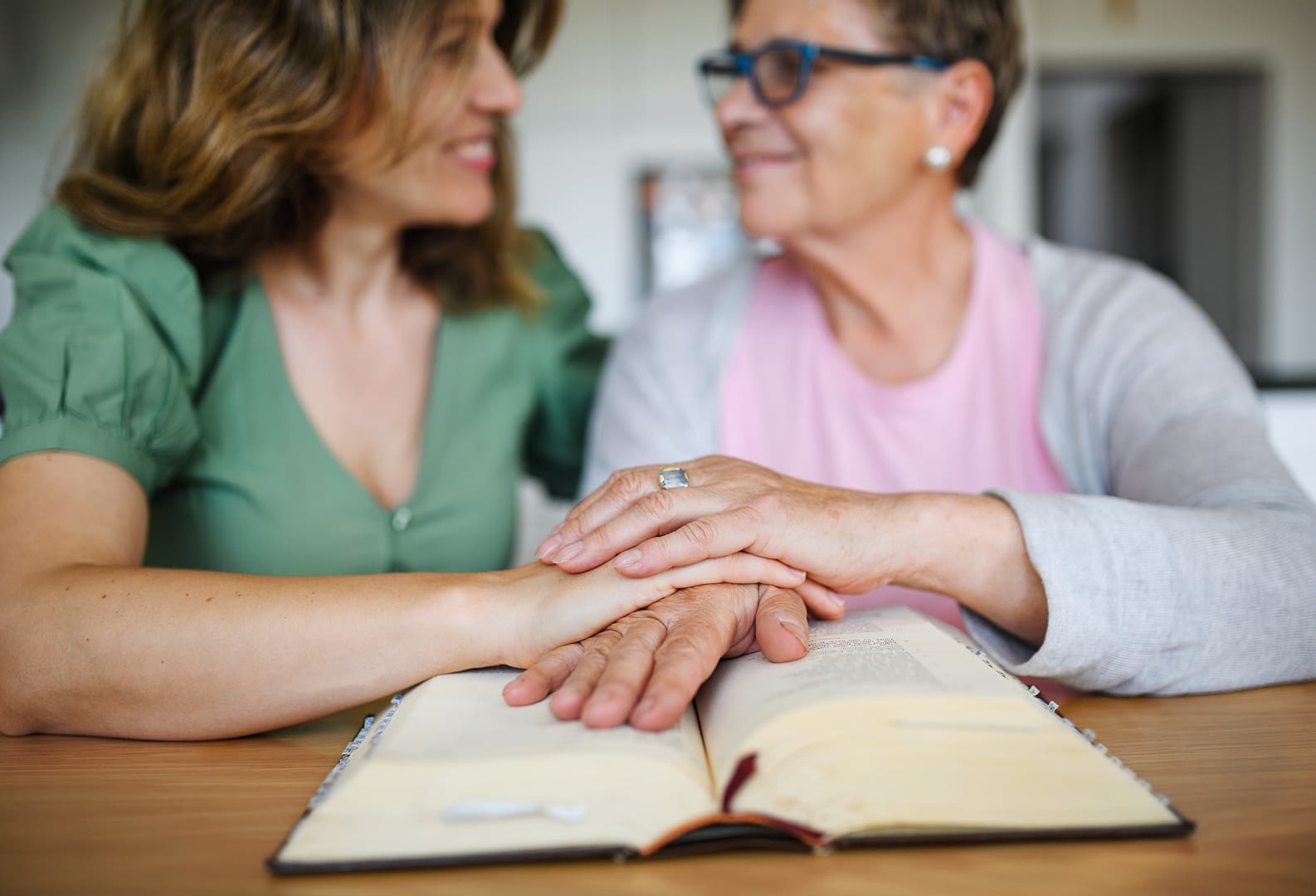Portrait of woman with senior mother indoors at home, reading bible.
