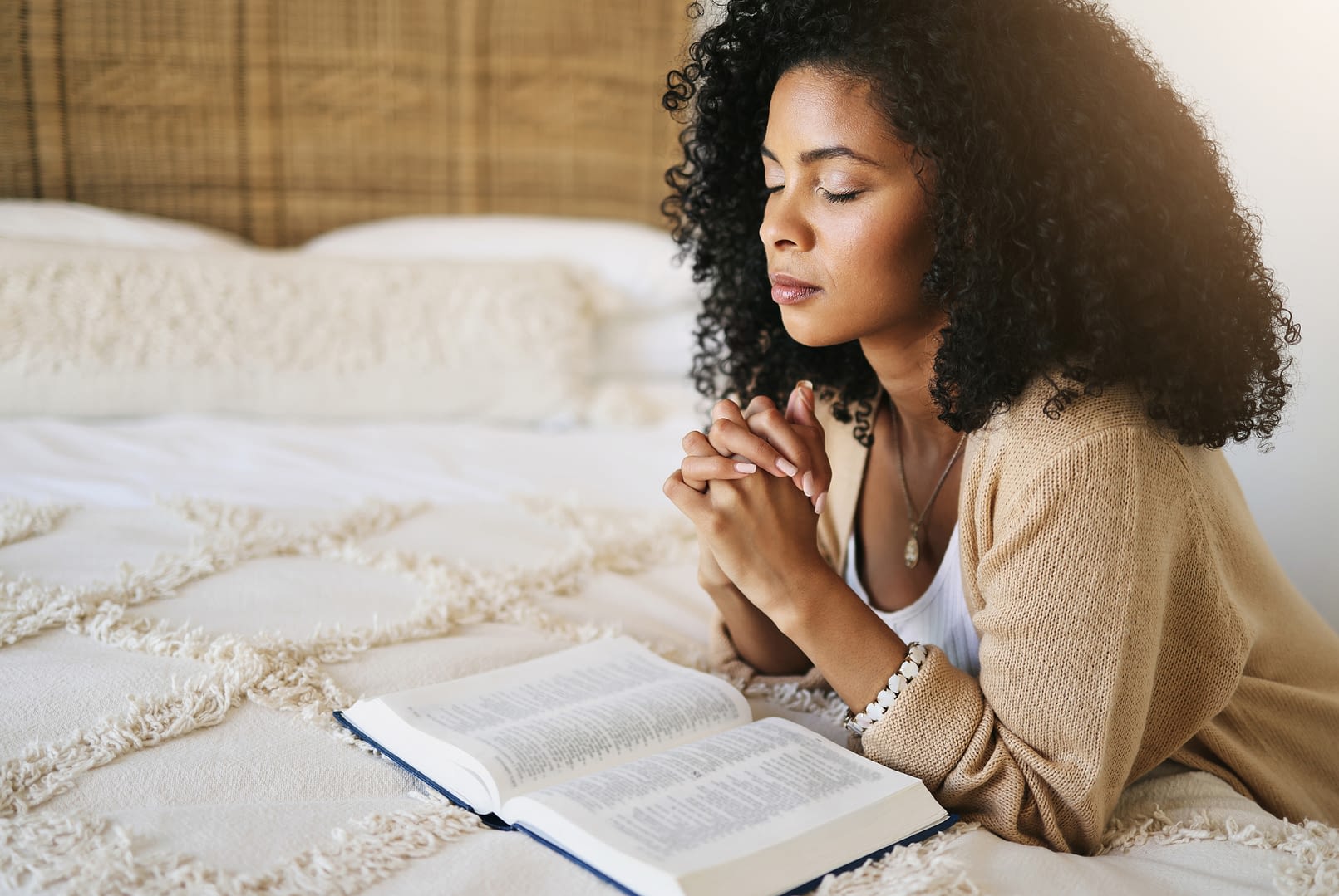 Bible, prayer and black woman praying on bed in bedroom home for hope, help or comfort in house.