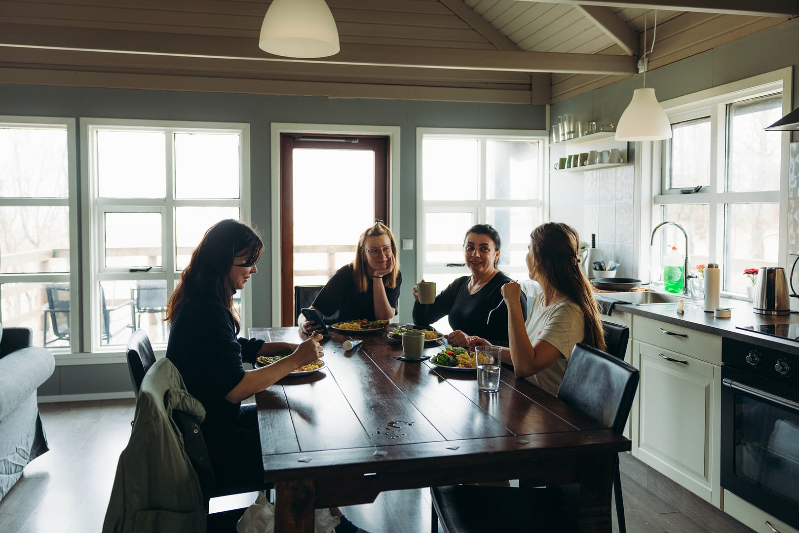 Cheerful multigenerational women enjoying weekend in the rural side in their summerhouse talking during breakfast in cozy atmosphere