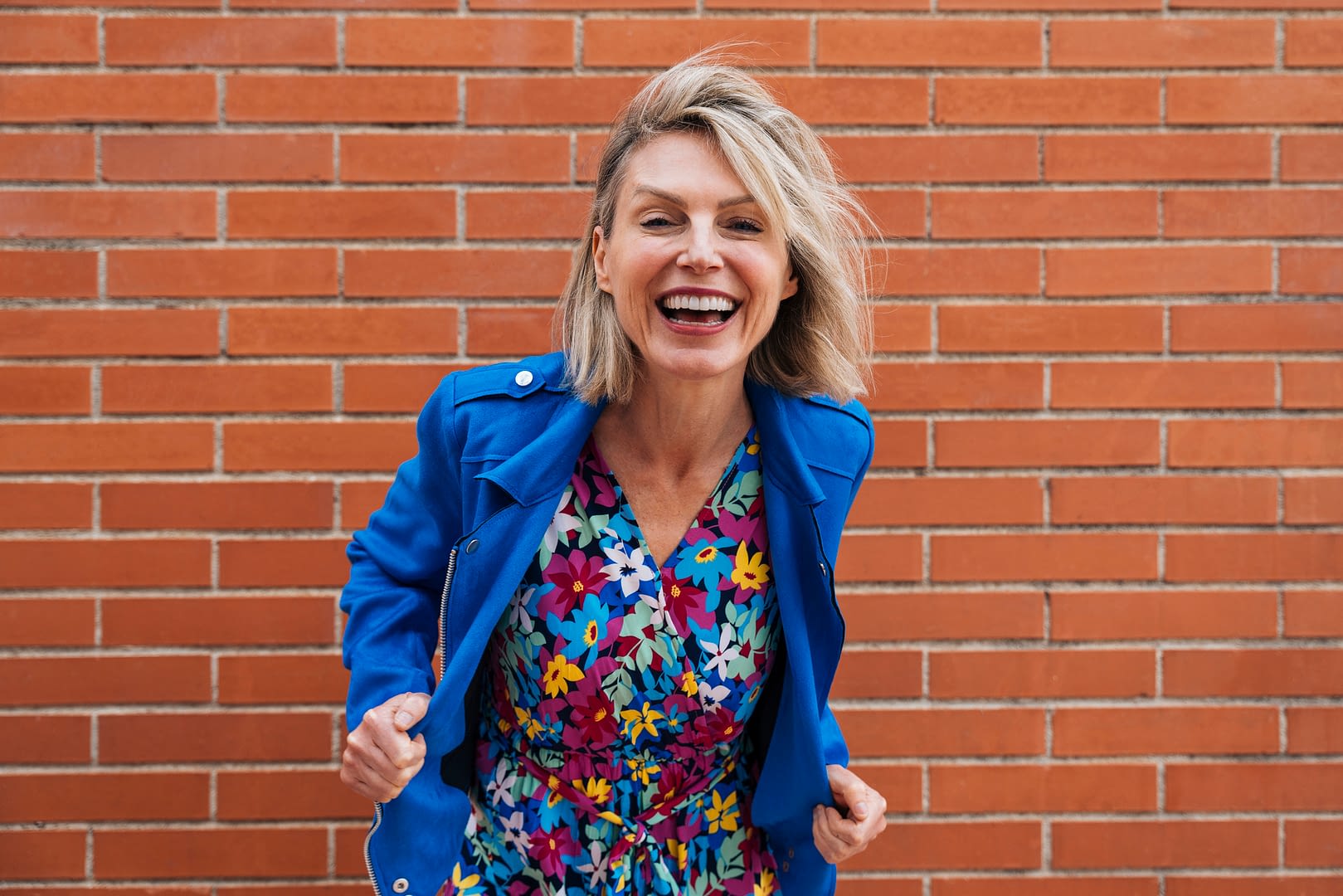 Smiling woman in colorful attire posing against a brick wall in an urban setting