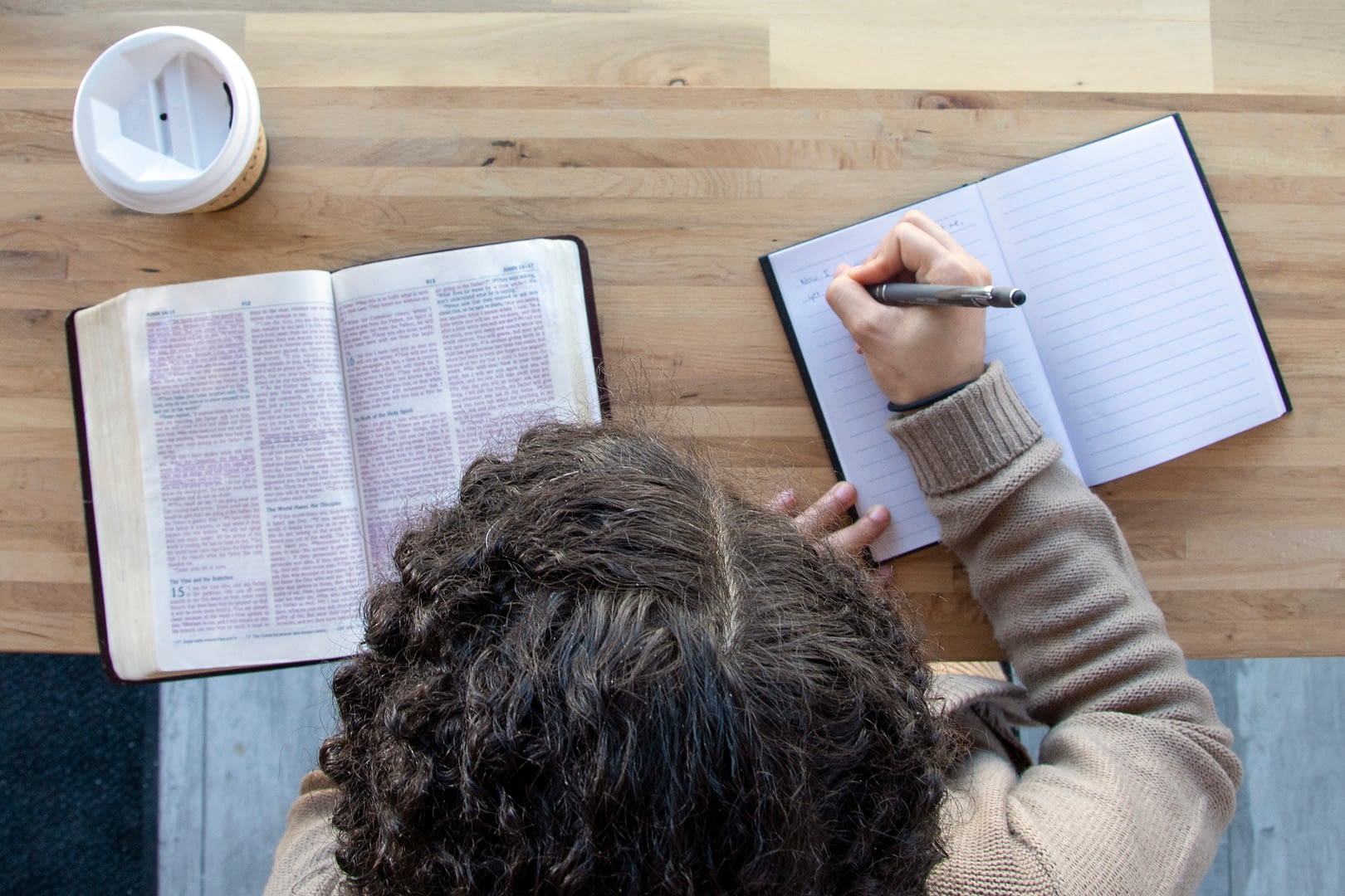 black woman sits and studying her bible with journal while drinking coffee