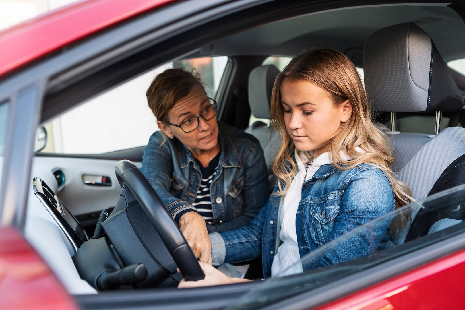 Mother teaching teenager to drive with concerned expression.