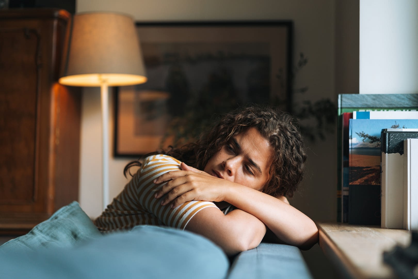 Depressed woman with curly hair sitting on sofa in room at home