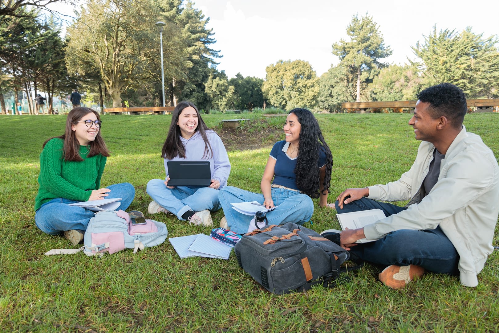 Young College Students Collaborating on Study Projects While Sitting on Grass.