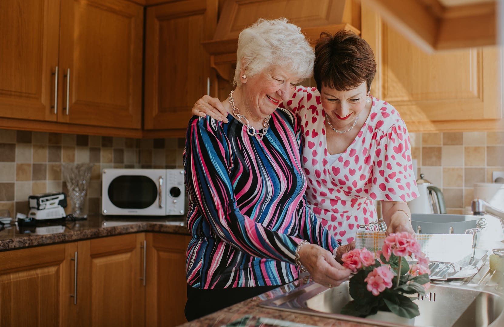 An older woman looks at some flowers with her elderly mother - a tender moment together