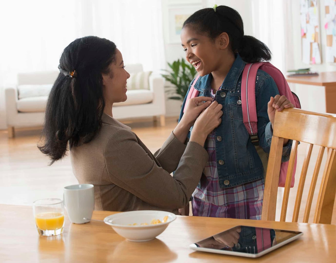 mother fastening jacket of daughter at breakfast table