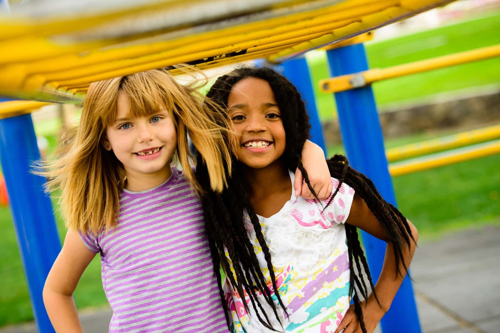 two girl friends smiling with arms around each other on the playground