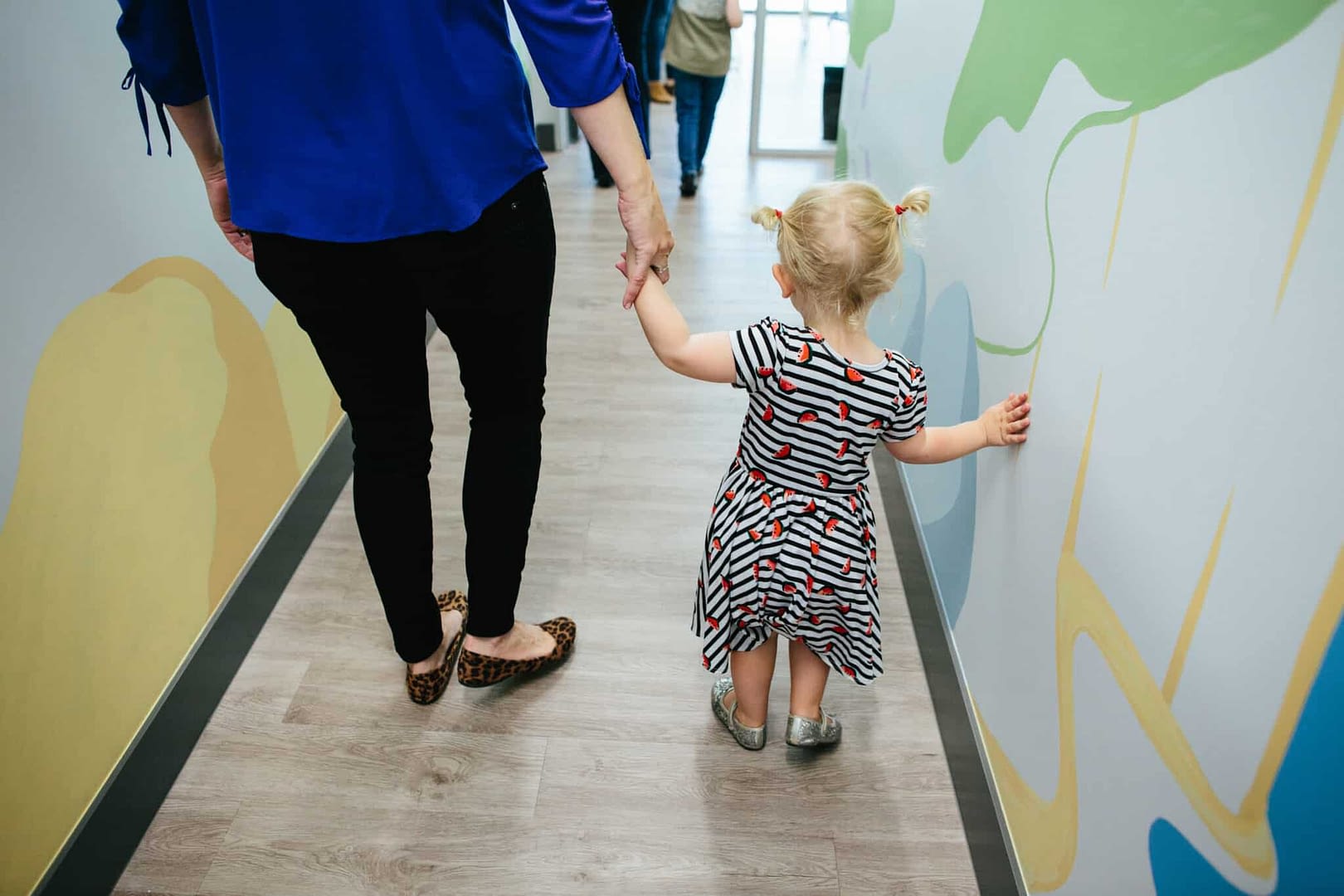 The backs of toddler girl and woman holding hands while walking