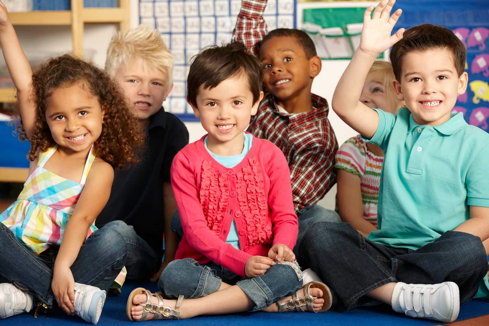 preschool kids raising their hands while sitting on the floor