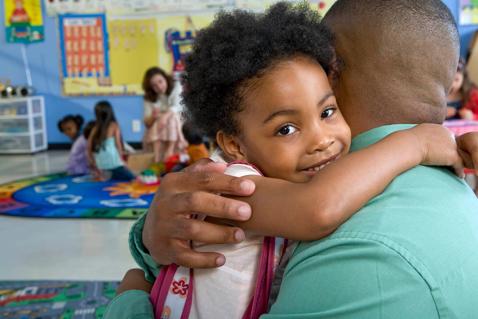Girl (4-5) embracing father in classroom while saying goodbye at dropoff
