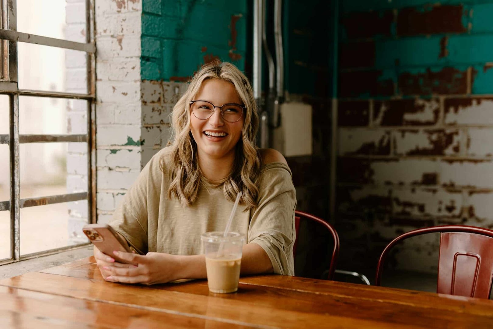 happy young adult woman smiling at table with phone in her hand