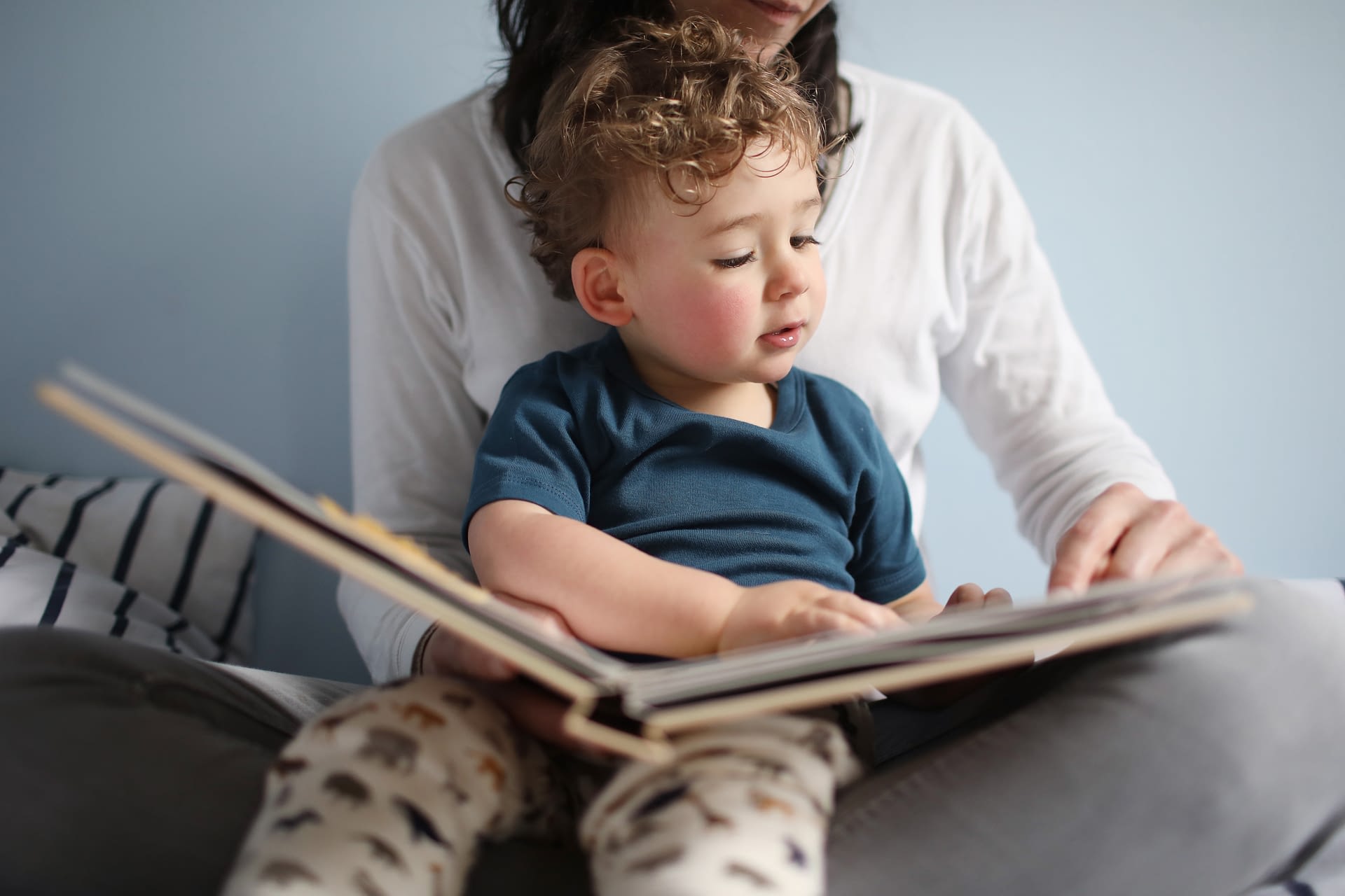 toddler reading a book on mom's lap